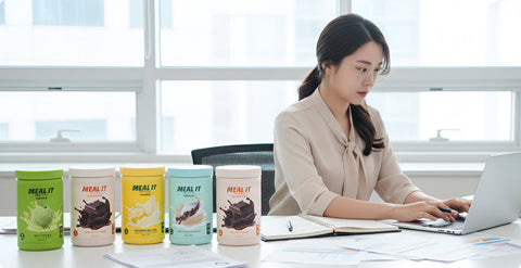 a woman workin with 5 variants of meal it protein shake displayed